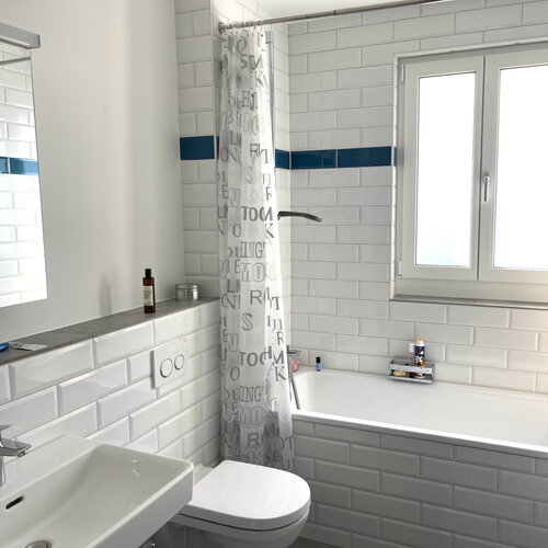 Badezimmer mit weissen Metro Bricks und einer blauen Bordüre fachmännisch angebracht. Helles und modernes Bad welches pflegeleicht und schön anzusehen ist.