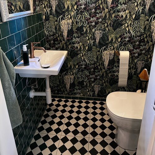 Kleines WC für Gäste mit Keramikboden in schwarz/weiss Schachbrett Muster. Passend dazu grüne Wandplatten und eine Dschungeltapete.