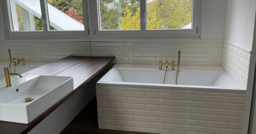 Badezimmer mit goldenen Armaturen passend zu dem warmen Keramikboden in Holzoptik und den leicht cremefarbenen Metrobricks an den Wänden.