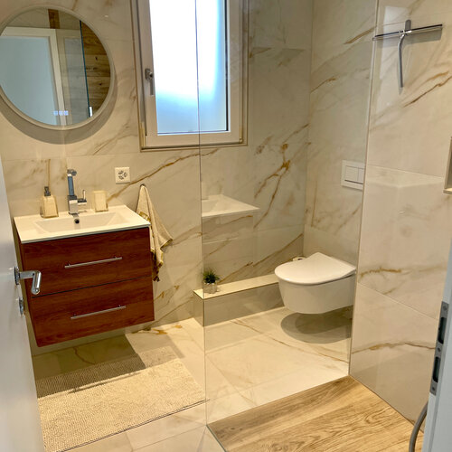 Kleine Dusche mit WC mit Keramik in Marmoroptik, kleinem Waschtisch aus Holz passend dazu.