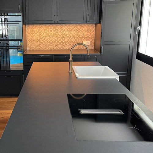 Moderne schwarze Küche mit Feinsteinzeug Abdeckung im Lederlook. Passend dazu ein Dekorküchenschild als besonderes Highlight du den schwarzen Fronten.
