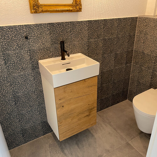 Wc mit blauen floralem Dekorplatten aus Keramik mit schwarzen Sanitärarmaturen.