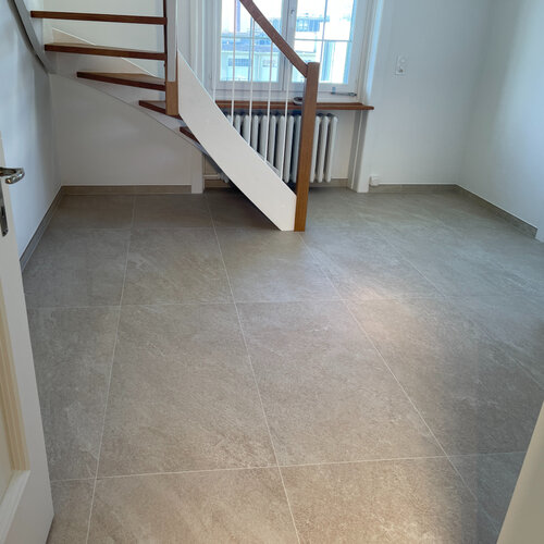 Eingang in einem EFH mit einer geschwundenen Treppe trifft auf Keramik in Quarz Optik in warmem beige.